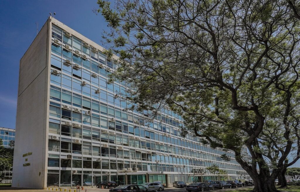 Edifício do Ministério da Fazenda em Brasília, com fachada de vidro e árvore em primeiro plano